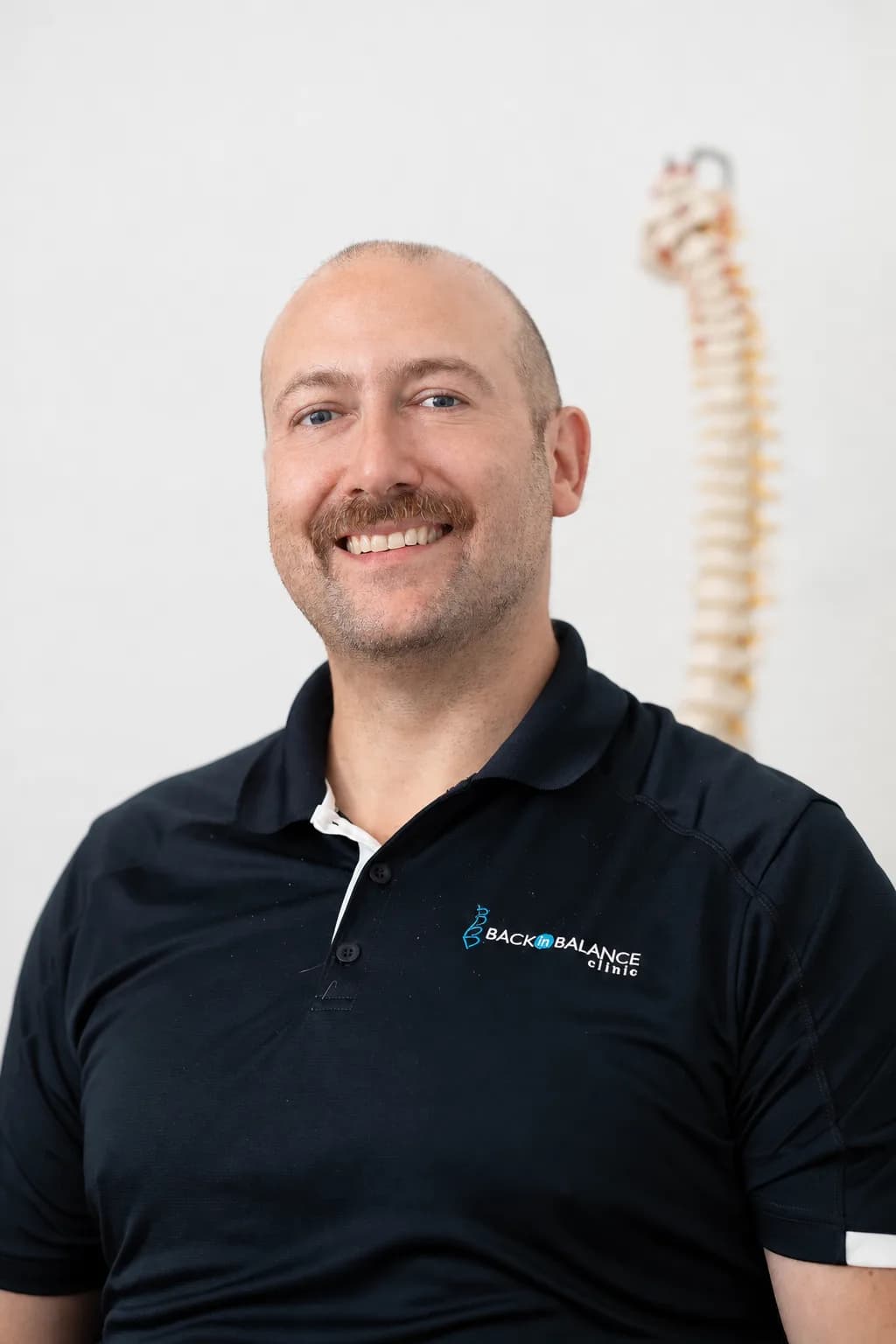 Dr. Matt, chiropractor at Back in Balance Clinic, smiling in a professional headshot with a spine model in the background